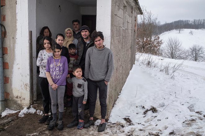 Družine priseljencev iz Iraka in Afganistana stojijo pred zapuščeno hišo, kjer živijo v vasi Hadzin Potok blizu severozahodnega mesta Velika Kladusa, Bosna in Hercegovina, 12. januarja 2021. FOTO: REUTERS/Marko Djurica